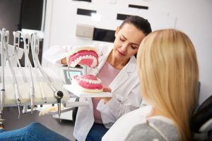 female-dentist-showing-patient-the-artificial-dent-EW9B8QG