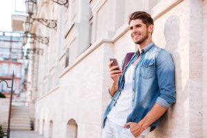 Smiling happy casual man using mobile phone outdoors