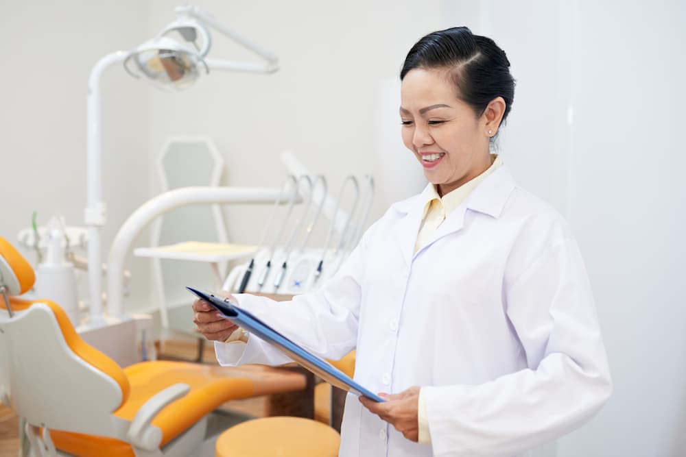 smiling-dentist-reading-clipboard-in-office-JN4YAUV (1)